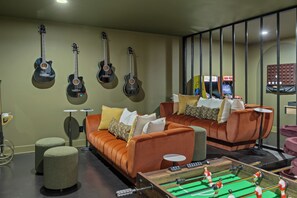 A room with a sofa, ottoman, and a foosball table. - Juniper & Jukebox - Movie Room, Rooftop w/ Mural & Fire Pit, 5 Bedrooms, 9 bed (Nashville)