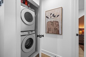 A laundry room with a Samsung washer and dryer, a door with a handle, and a painting on the wall. - Juniper & Jukebox - Movie Room, Rooftop w/ Mural & Fire Pit, 5 Bedrooms, 9 bed (Nashville)