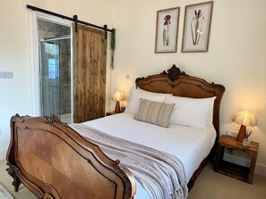 Ein Schlafzimmer mit einem großen Bett, zwei Nachttischen mit Lampen, einer Schiebetür und zwei gerahmten Pflanzenbildern an der Wand.