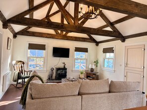 A cozy living room with a high wooden ceiling, a fireplace, a sofa, and a television. - Gorse Cottage Connemara | Wild Atlantic Way | Sleeps 4 | Pet Friendly (Cashel)