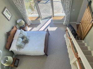 A bedroom with a bed, pillows, a nightstand, a lamp, a window with curtains, and a staircase. - Lios an Uisce Cottage Connemara | Wild Atlantic Way | Sleeps 6 | Pet Friendly (Cashel)