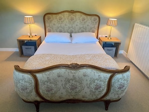 A bed with a floral-patterned headboard and footboard, flanked by two bedside tables with lamps, in a room with a carpeted floor. - Lios an Uisce Cottage Connemara | Wild Atlantic Way | Sleeps 6 | Pet Friendly (Cashel)
