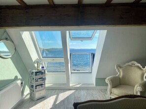 Una habitación con vista al mar, un sillón antiguo y una mesita con lámpara.