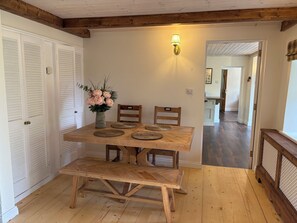 A wooden dining table with four chairs, a vase of flowers, and a wall-mounted light fixture in a room with wooden floors and white walls. - Mayfly Cottage in Oughterard | Wild Atlantic Way | Sleeps 6 | Pet Friendly (Cashel)