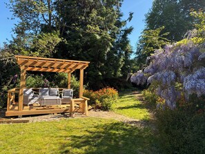 A wooden pergola with seating, surrounded by lush greenery and flowering plants. - Mayfly Cottage in Oughterard | Wild Atlantic Way | Sleeps 6 | Pet Friendly (Cashel)