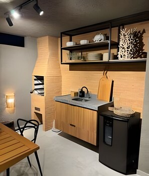 Eine kleine Küche mit einer Holzausziehtafel, einem schwarzen Kühlschrank und einem Esstisch mit Stühlen.