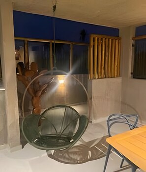 Ein Zimmer mit einem Glaskugelstuhl, einem Holztisch und Blick ins Freie.