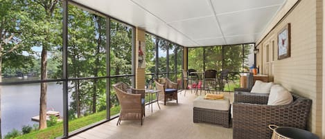A covered outdoor area with wicker furniture, a view of a lake, and a brick wall.