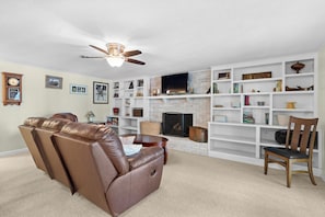 A living room with a fireplace, a ceiling fan, and a bookshelf. - Hillview Lakefront Retreat w/ Private Pier (Lexington)