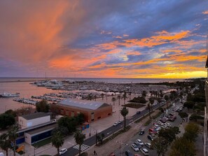 A marina with boats docked, a building with a flat roof, and a road with parked cars. - Luxury Penthouse with Panoramic Sea Views (Vilanova i la Geltru)