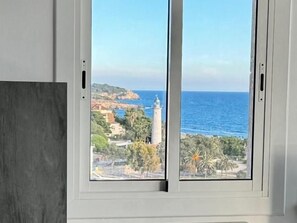 A window with a view of a coastal landscape, including a lighthouse and buildings. - Luxury Penthouse with Panoramic Sea Views (Vilanova i la Geltru)