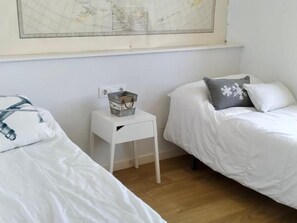A bedroom with two single beds, a small white nightstand with a metal bucket, and a large map on the wall. - Luxury Penthouse with Panoramic Sea Views (Vilanova i la Geltru)