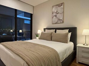 Ein modernes Schlafzimmer mit einem großen Bett, Nachttischlampen, Blick durch ein Fenster und einer Wanddekoration.