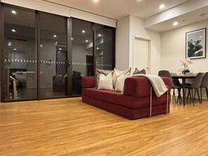 Ein modernes Wohnzimmer mit einem roten Sofa, einem Esstisch mit Stühlen und einer Schiebetür zu einem weiteren Raum.