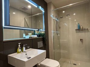 Ein modernes Badezimmer mit Duschkabine aus Glas, einem weißen Waschbecken und einem großen Spiegel.