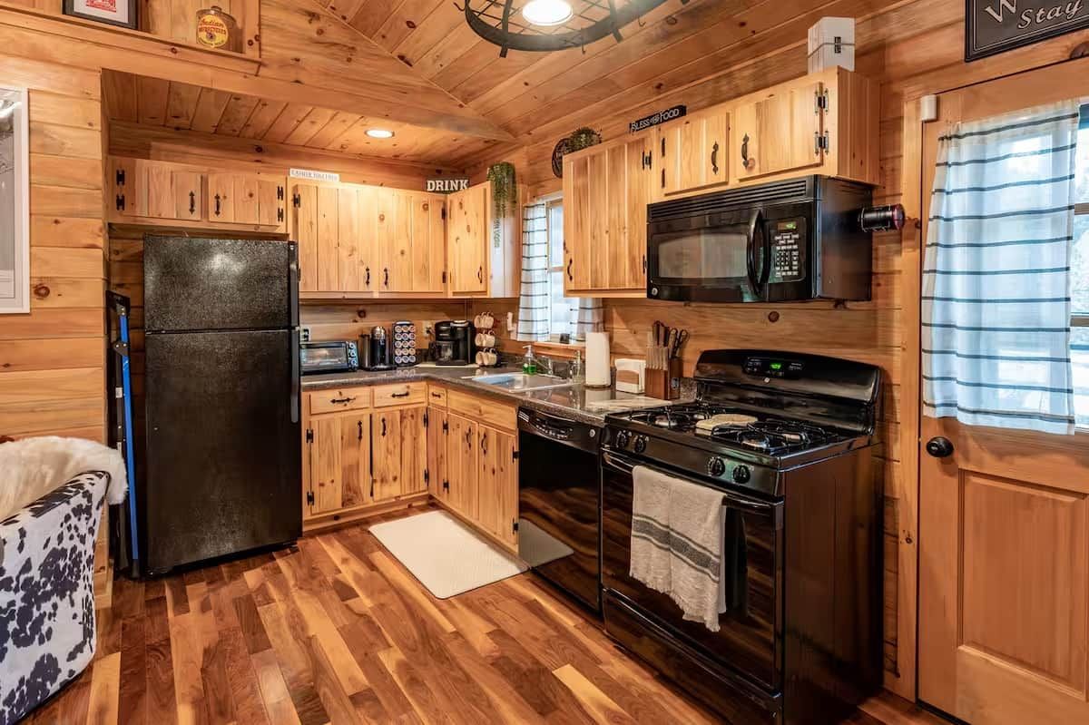 A cabin-style kitchen with wooden cabinets, a refrigerator, a microwave, a stove, and a sink.