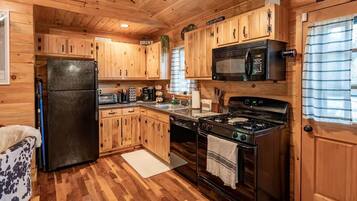 A cabin-style kitchen with wooden cabinets, a refrigerator, a microwave, a stove, and a sink.