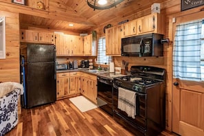 A cabin-style kitchen with wooden cabinets, a refrigerator, a microwave, a stove, and a sink.