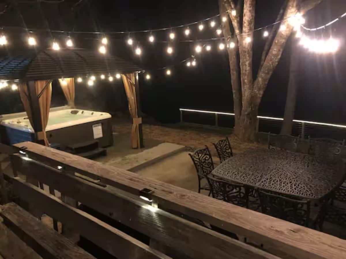 Un patio al aire libre con luces colgantes, un jacuzzi y una mesa con sillas.