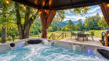 Un jacuzzi con vistas a un paisaje montañoso, mobiliario exterior y luces colgantes.