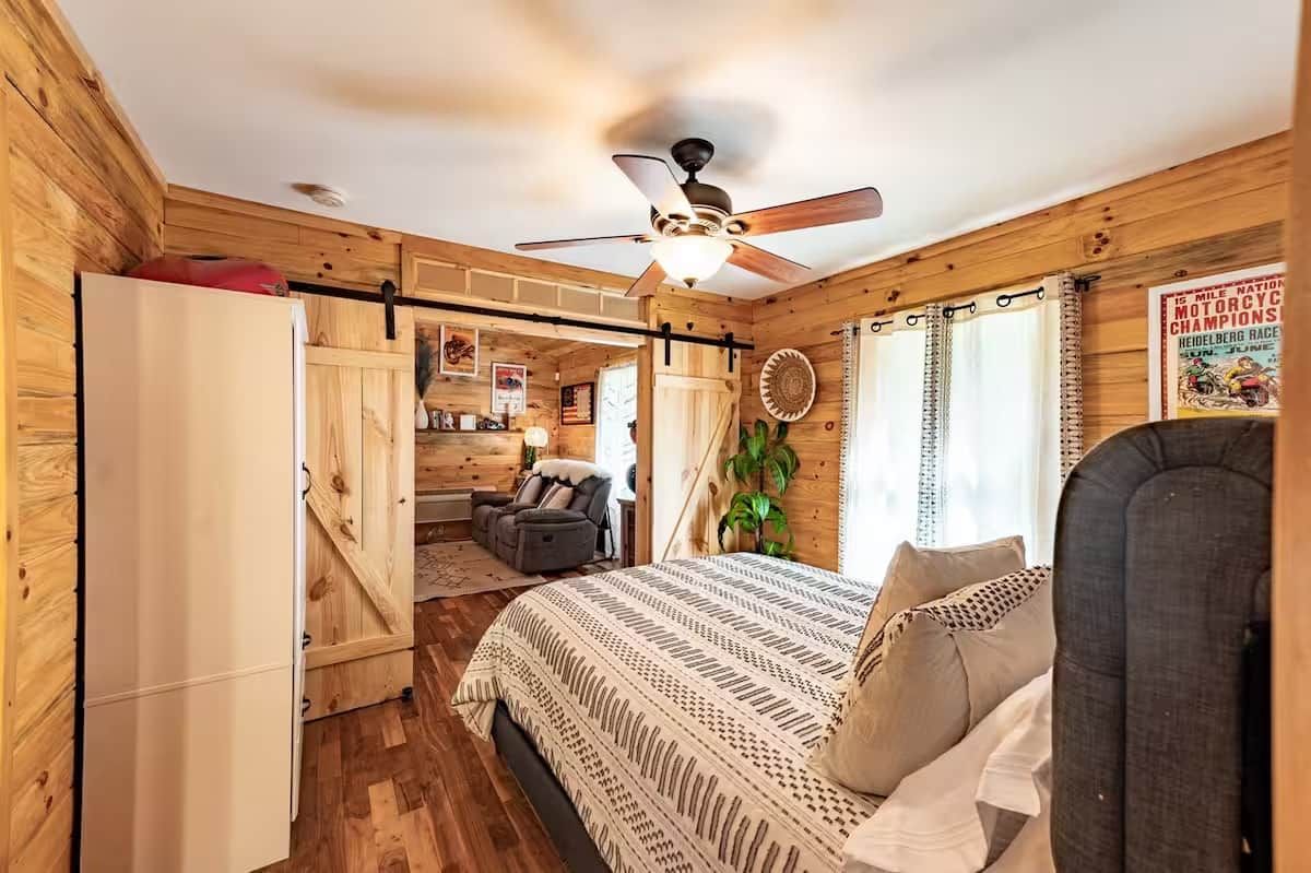 A cozy cabin-style room with a bed, a ceiling fan, a dining area, and a kitchen.