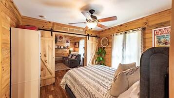A cozy cabin-style room with a bed, a ceiling fan, a dining area, and a kitchen.