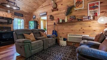 A cozy cabin interior with a fireplace, wooden walls, a dining area, and a seating area with a fireplace.