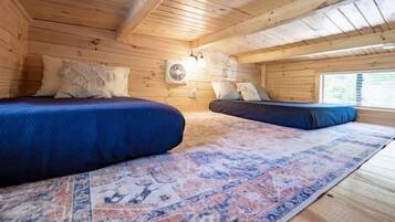 A cabin with two beds, a patterned rug, wooden walls, and a window.