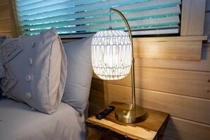 A bed with a remote control on a wooden bedside table next to a wall with horizontal blinds. - Humble Roots Hideout-  Near Tail of the Dragon & Cherohala Skyway (Graham County)
