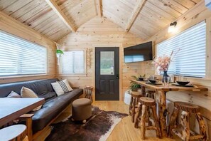 Et hyggeligt interiør med træloft, en sofa, et spisebord med barstole og et fjernsyn ophængt på væggen.