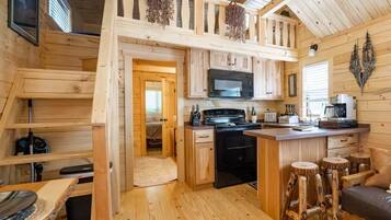 A wooden cabin interior with a kitchen area, a dining table, and a seating area.