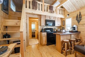 A wooden cabin interior with a kitchen area, a dining table, and a seating area. - Humble Roots Hideout-  Near Tail of the Dragon & Cherohala Skyway (Graham County)