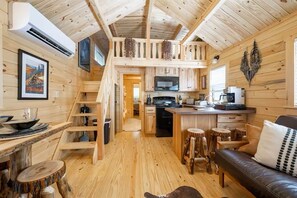 A wooden cabin interior with a kitchen, dining area, and a living room with a sofa and stools. - Humble Roots Hideout-  Near Tail of the Dragon & Cherohala Skyway (Graham County)