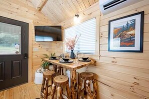 A wooden interior with a dining table, stools, a mounted TV, and a framed picture on the wall. - Humble Roots Hideout-  Near Tail of the Dragon & Cherohala Skyway (Graham County)