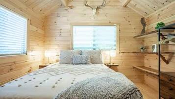 Quarto de cabana de madeira com cama, duas mesas de cabeceira e janela.