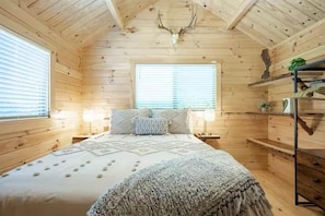 A wooden cabin bedroom with a bed, two bedside tables, and a window.