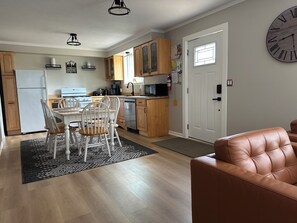 Eine moderne Küche mit Holzausbau, eine Essecke mit weißem Tisch und Stühlen, und ein braunes Ledersofa.