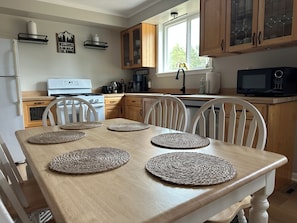 A kitchen with wooden cabinets, a white stove, and a dining table with woven placemats. - Cozy Cabin/ORV/Fishing/Fire Pit/Dog Friendly (Irons)
