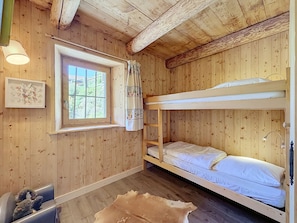 A wooden cabin room with a bunk bed, a window with curtains, a framed picture, and a leather hide on the floor. - Chalet Mont-Blanc view - 6 guests (Combloux)
