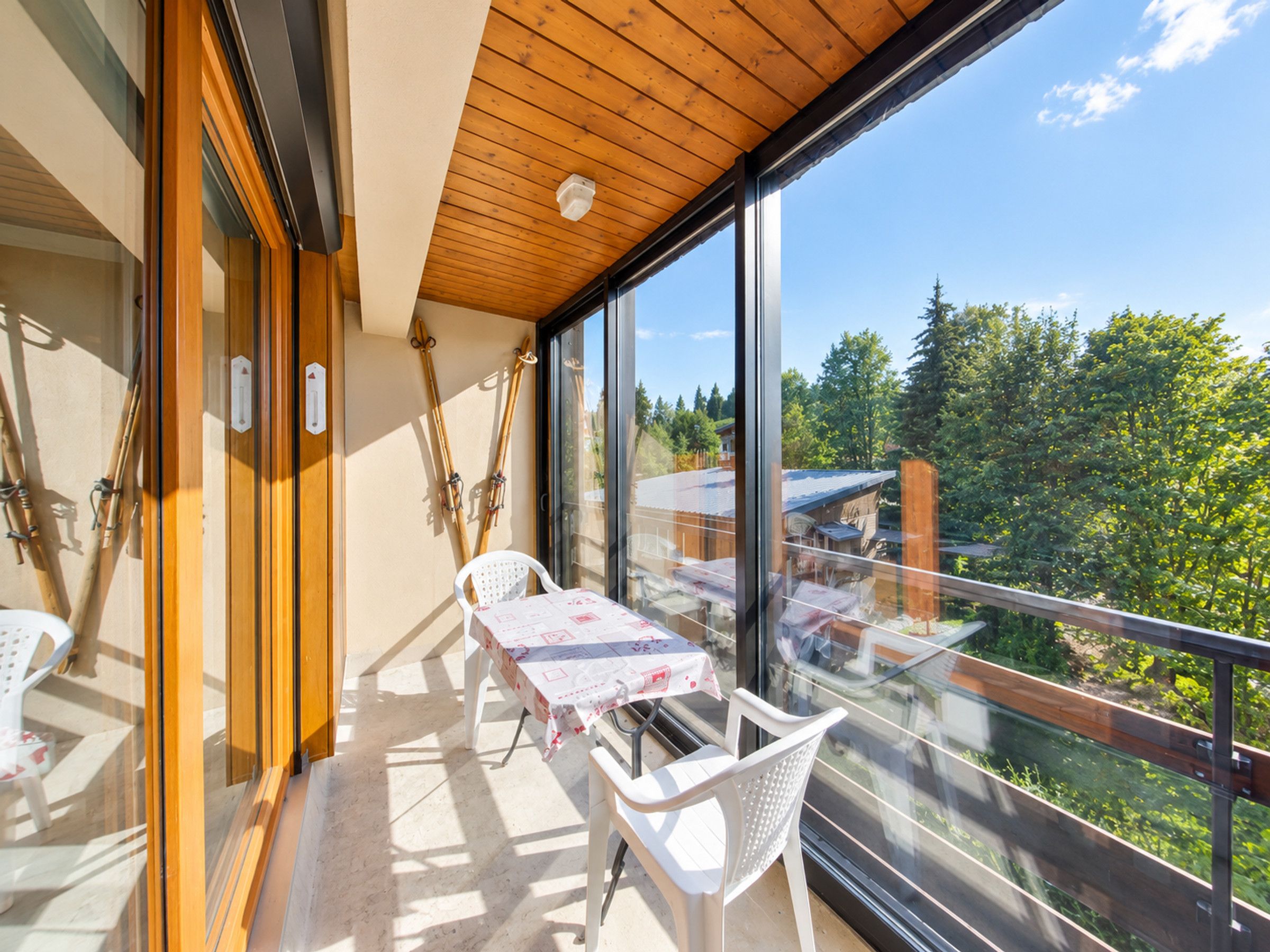 A balcony with a table and chairs, a wooden ceiling, and a view of trees and buildings.