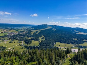A mountainous landscape with a clear sky, dense forests, and a small settlement with visible roads and buildings. - Apartment for 2 near Les Rousses center (Les Rousses)