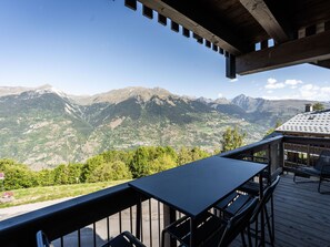 A wooden deck with a table and chairs, overlooking a mountainous landscape. - Spacious apartment with mountain view - 10 guests (La Plagne Montalbert)
