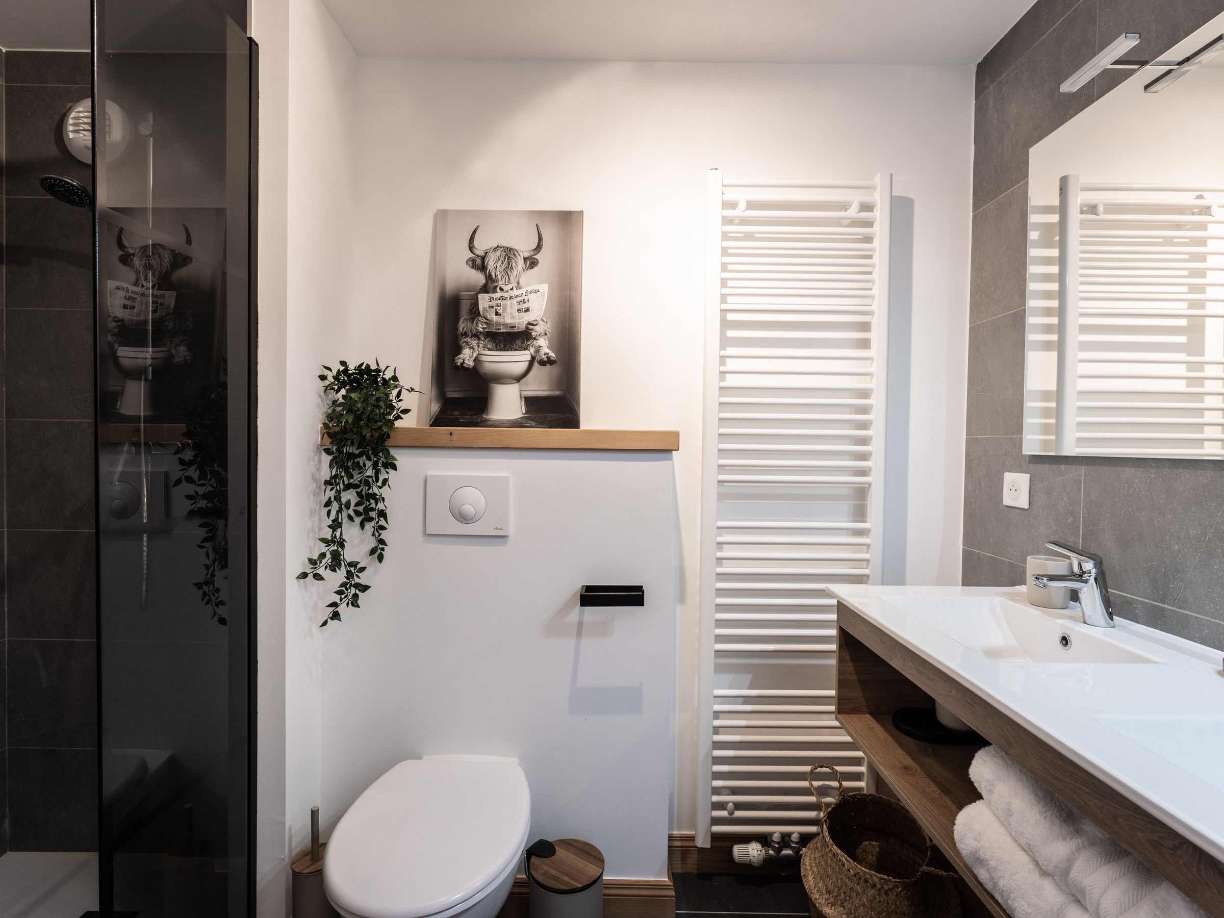 A modern bathroom with a toilet, a sink, a mirror, a radiator, and a shower area.