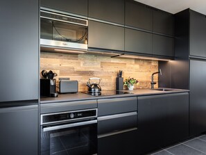 A modern kitchen with stainless steel appliances, a wooden backsplash, and a black countertop. - Spacious apartment with mountain view - 10 guests (La Plagne Montalbert)