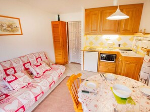 A compact kitchen with wooden cabinets, a small refrigerator, and a dining table set for two. - Charming apartment with mountain view - 4 guests (Villarodin-Bourget)