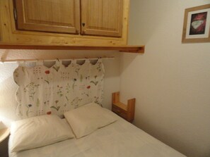 A bedroom with a bed, a wooden cabinet above, a floral curtain, and a framed picture on the wall. - Charming apartment with mountain view - 4 guests (Villarodin-Bourget)