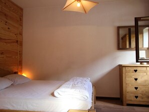 A bedroom with a wooden bed, a wooden dresser with heart-shaped handles, and a mirror on the wall. - Apartment mountain view - 4 guests (Villarodin-Bourget)