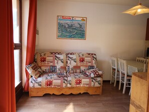 A cozy living room with a patterned sofa, a dining table with chairs, and a wall-mounted painting. - Apartment mountain view - 4 guests (Villarodin-Bourget)