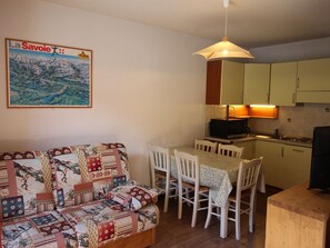 Ein gemütlicher Wohnbereich mit Sofa, Esstisch, Stühlen und einer Küche mit Mikrowelle.