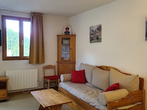 A cozy living room with a sofa, a wooden cabinet, a radiator, and a window with curtains. - Pleasant apartment pets welcome - 6 guests (Valfréjus)